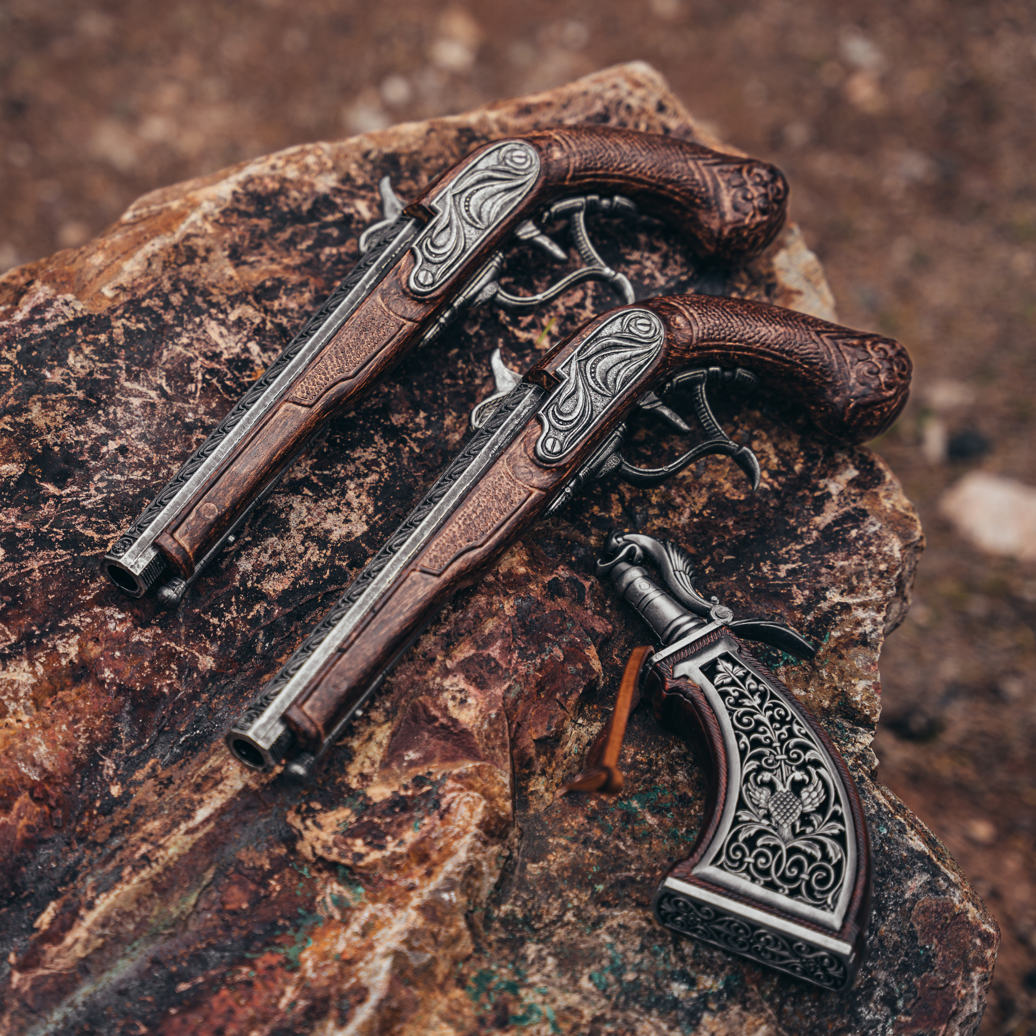 two pirate dueling flintlocks with ornate powder horn sitting on a rock