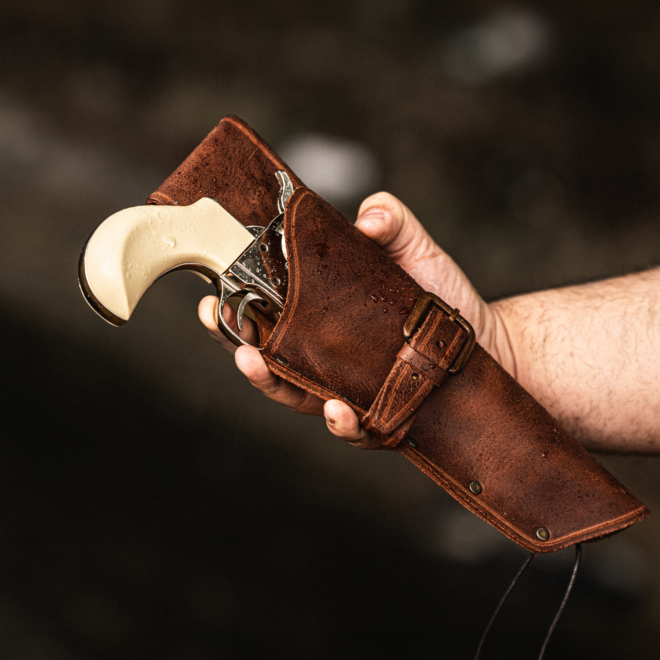 Hand holding leather Colt holster with pearl handled Thunderer revolver inside