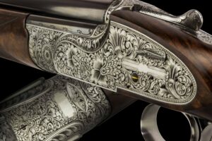 A close-up view of an intricately engraved shotgun, showcasing detailed floral and scrollwork patterns on the metal parts