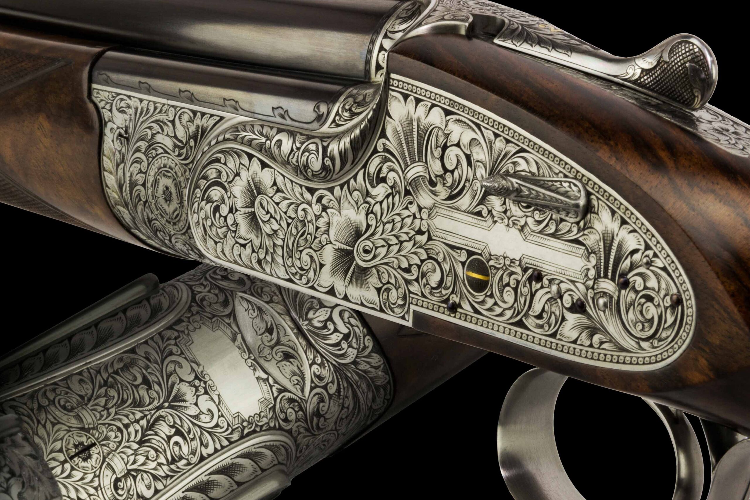 A close-up view of an intricately engraved shotgun, showcasing detailed floral and scrollwork patterns on the metal parts
