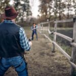 Two cowboys face off in a duel on a dirt path lined with a wooden fence, surrounded by trees.