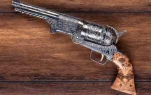 An intricately engraved antique revolver with a wooden grip, displayed on a wooden surface.