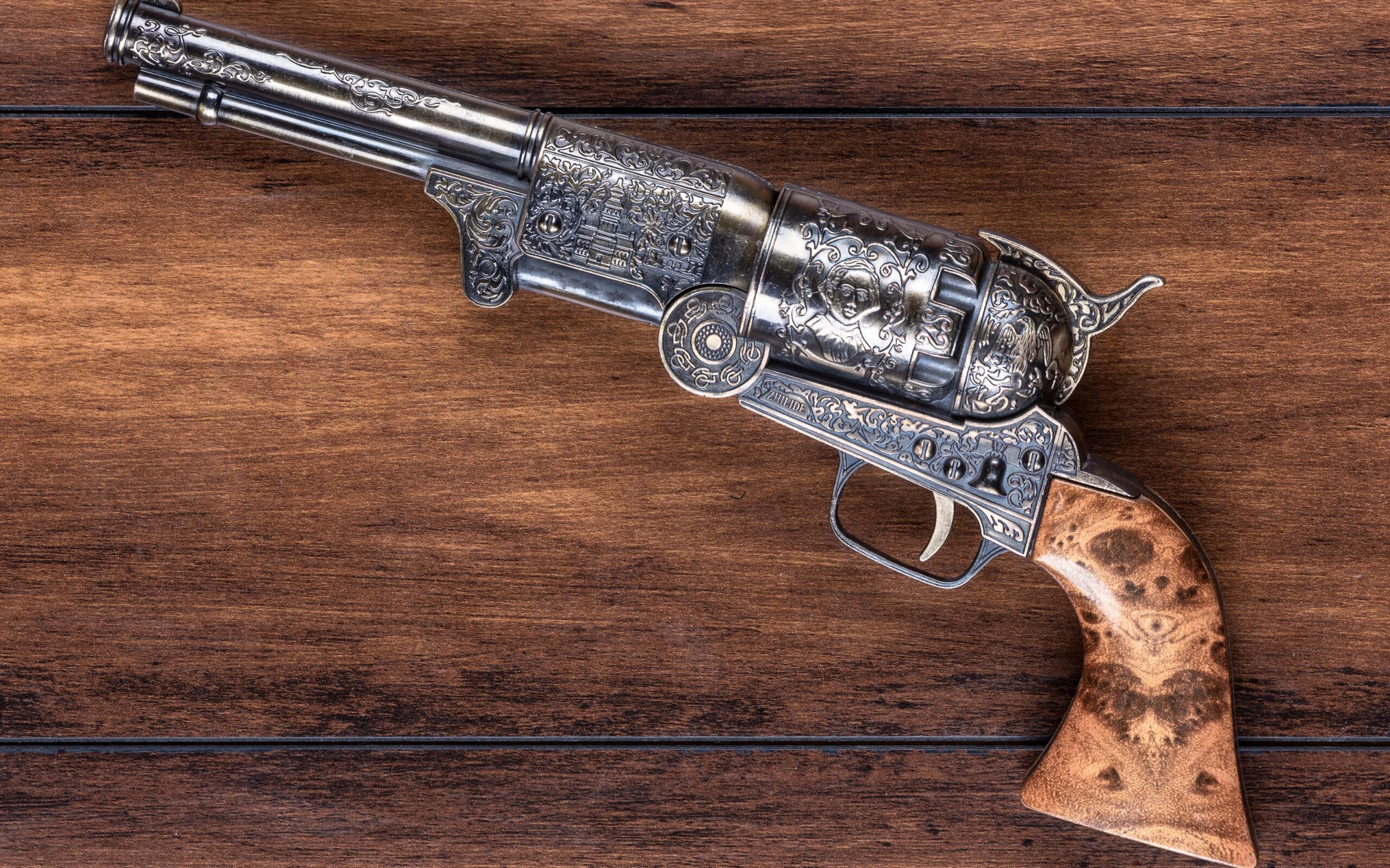 An intricately engraved antique revolver with a wooden grip, displayed on a wooden surface.