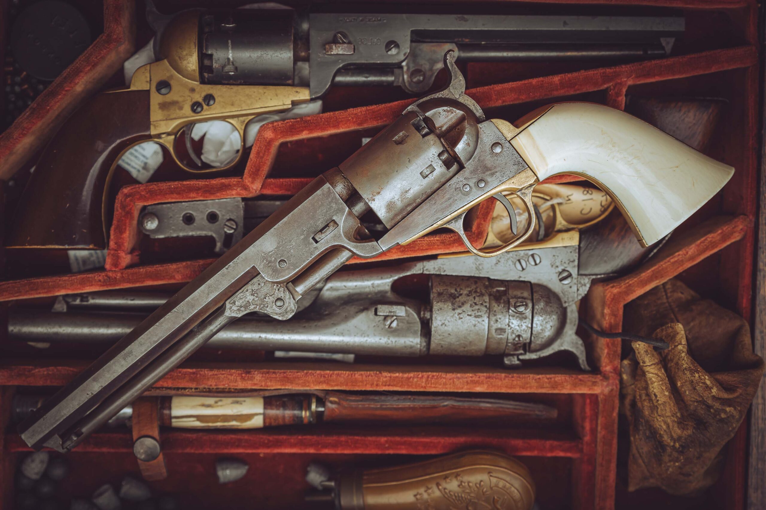 A collection of vintage revolvers displayed in a red velvet-lined case