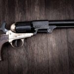 Vintage revolver with wooden grip and long barrel on a dark wooden surface