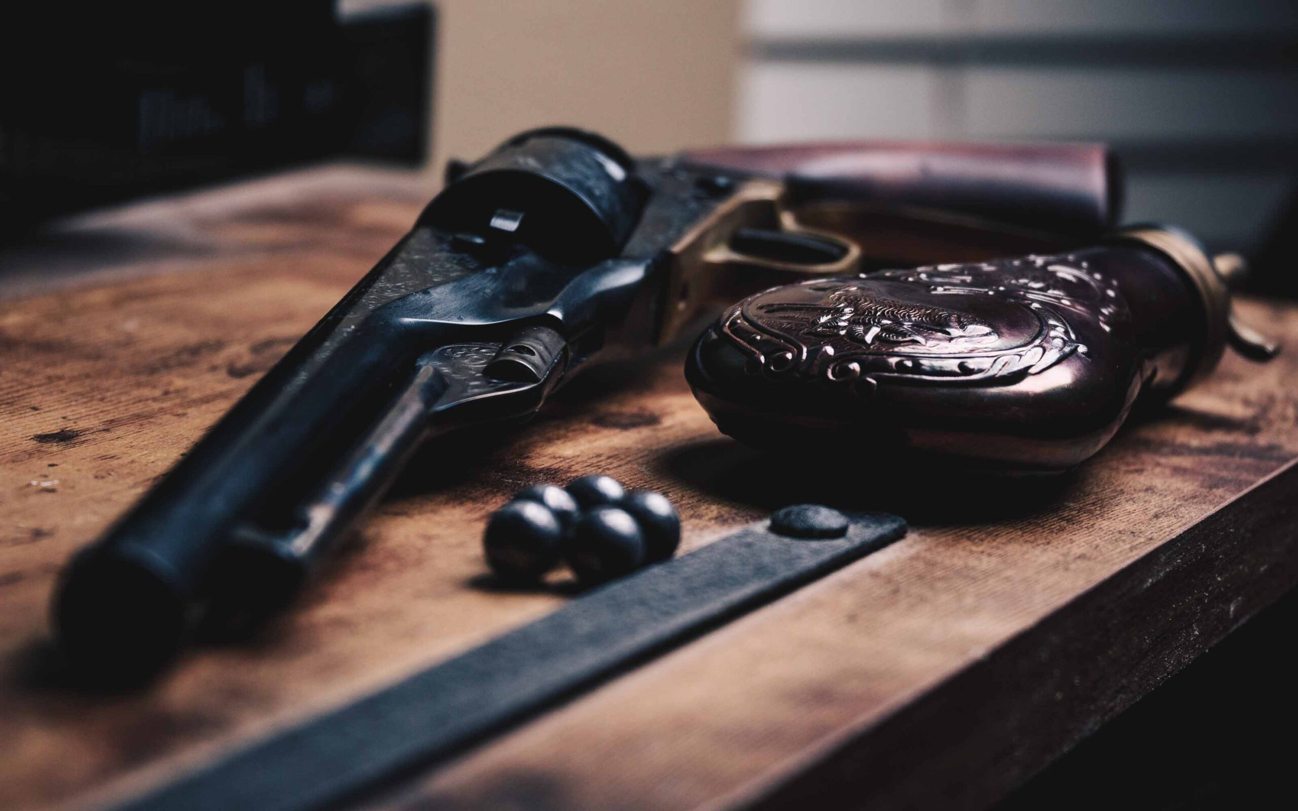 -up of an old-fashioned revolver, ornate powder flask, lead balls, and metal tool on a wooden surface
