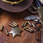 Vintage revolver, rifle, bullets, sheriff badge, cowboy hat, and coins arranged on a wooden table, symbolizing the Old West.