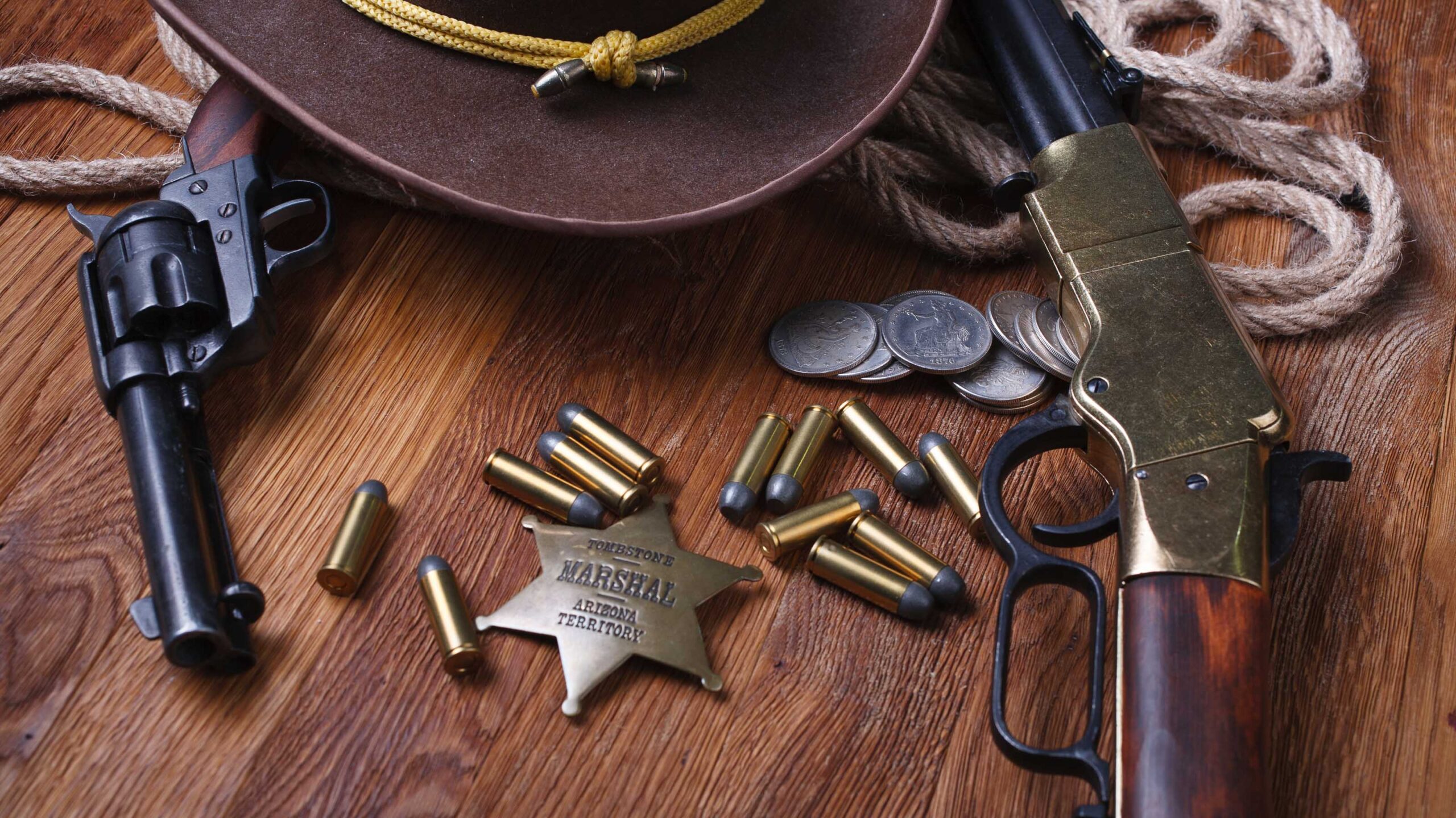 Vintage revolver, rifle, bullets, sheriff badge, cowboy hat, and coins arranged on a wooden table, symbolizing the Old West.