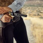 Cowboy in the Old West drawing a revolver from his holster while standing on a desert trail.