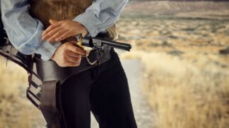 Cowboy in the Old West drawing a revolver from his holster while standing on a desert trail.