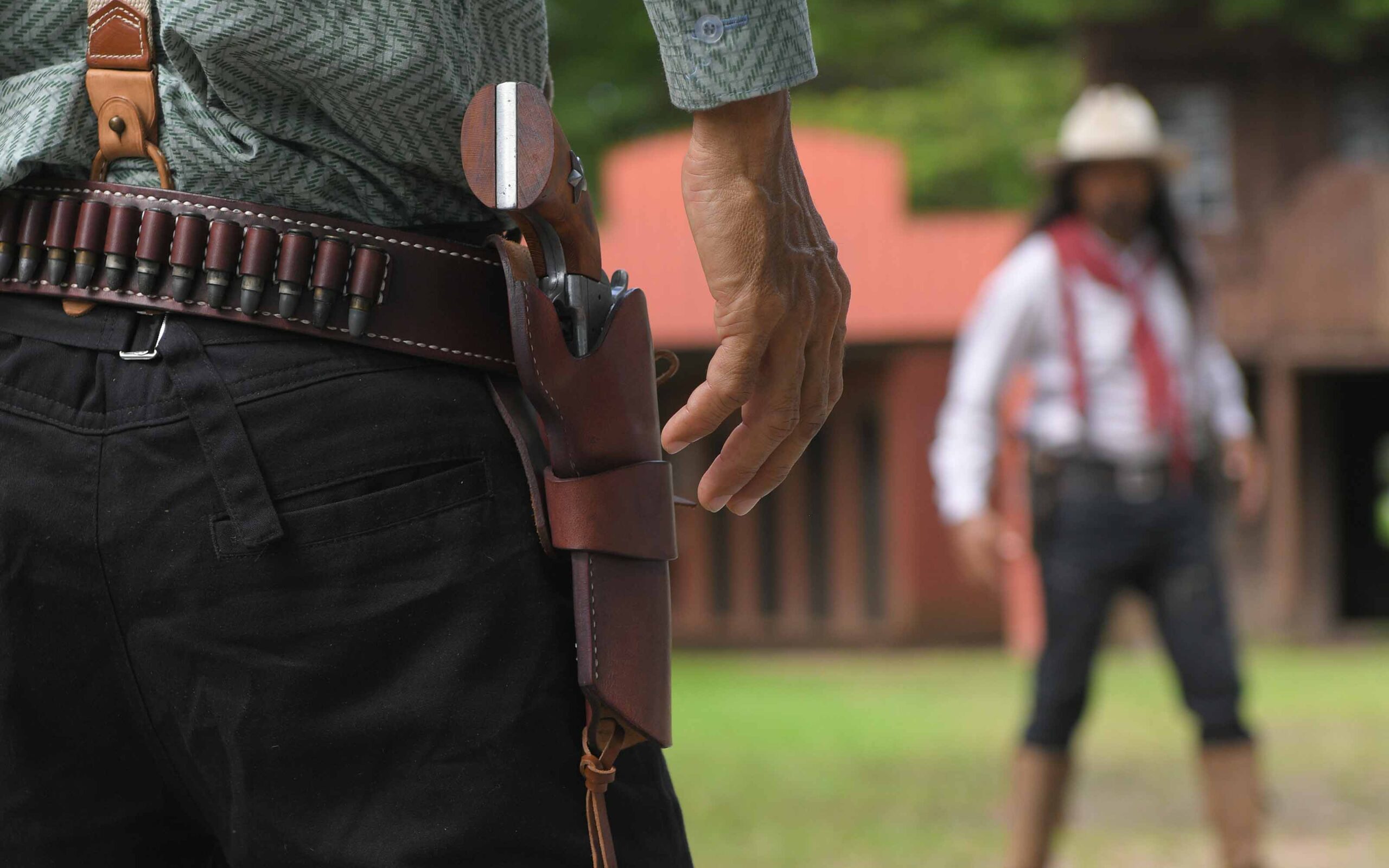A close-up of a historical reenactor in a cowboy costume, his hand near a non-firing replica revolver holstered in a leather gun belt.